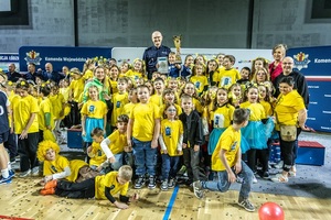 Zmagania dzieci podczas zawodów sportowych na sali gimnastycznej w obecności policjantów i aktorów.