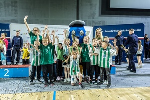 Zmagania dzieci podczas zawodów sportowych na sali gimnastycznej w obecności policjantów i aktorów.