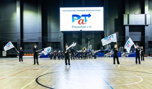 Młodzież w czarnych mundurach ćwiczebnych macha flagami z napisem PaT.