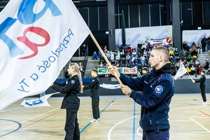 Młodzież w czarnych mundurach ćwiczebnych macha flagami z napisem PaT.