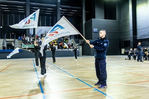 Młodzież w czarnych mundurach ćwiczebnych macha flagami z napisem PaT.