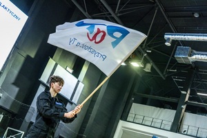 Młodzież w czarnych mundurach ćwiczebnych macha flagami z napisem PaT.