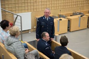 Umundurowany policjant stoi, przed nim znajdują się osoby siedzące na sali wykładowej.