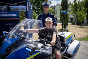 Dziecko siedzi na motocyklu w tle stoi policjant.