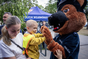 Dziecko przybija piątkę z maskotką policyjną.