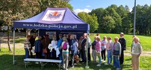 Namiot profilaktyczny z napisem policja łódzka, przed namiotem stoi grupa seniorów.