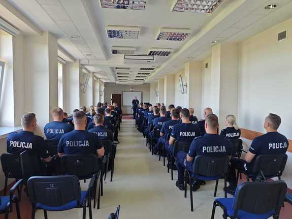 Policjanci w mundurach siedzą na sali wykładowej.