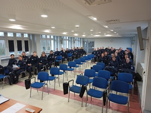 Słuchacze szkolenia siedzą w ławkach na sali.