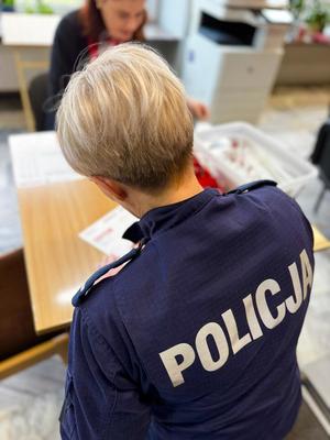 Poicjantka tyłem, wypełnia dokumenty.