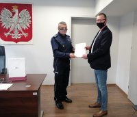 Komendant Miejski Policji w Piotrkowie Trybunalskim wręcza funkcjonariuszowi list z podziękowaniem, w tle godło Polski