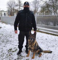 Na zdjęciu widać policjanta stojącego na śniegu oraz jego psa służbowego