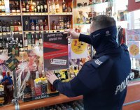 policjant przy ladzie sklepowej zawiesza plakat dotyczący zakazu sprzedaży alkoholu osobom niepełnoletnim.