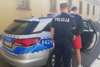 policjant prowadzi zatrzymanego do policyjnego radiowozu