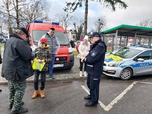 Policjant i młodzież z Młodzieżowej Grupy Pożarniczej podczas rozdawania odblasków