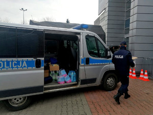 policjant wnoszący zebrane dary do miejsca w którym mają być przyjmowani uchodźcy