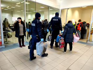 policjanci pomagający uchodźcom wnoszący ich bagaże