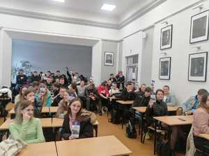 na zdjęciu uczniowie klasy maturalnej siedzą w ławkach trzymają w rękach ulotki informacyjne -jak zostać Policjantem