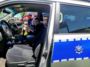 chłopiec siedzący w radiowozie policyjnym na fotelu pasażera, za nim widać policjanta