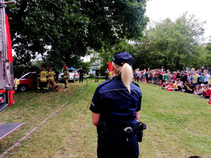 dzielnicowa podczas policyjnego pikniku przygląda się symulacji akcji ratowniczej prowadzonej przez funkcjonariuszy straży pożarnej