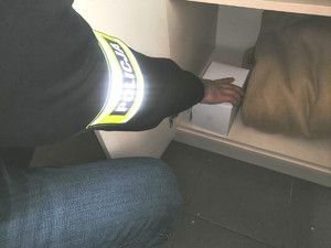 na zdjęciu policjant sięga do szafki po pudełko , w którym odnajduje skradzione mienie