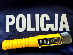 Urządzenie do badania stanu trzeźwości, nad nim napis Policja na policyjnym mundurze.