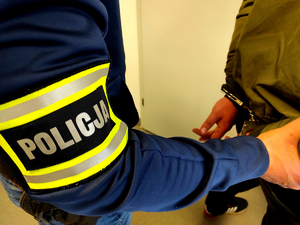 policjant trzymający ręce zatrzymanego, który ma założone kajdanki.