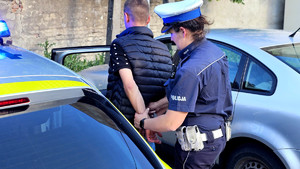 Policjantka podczas zakładania kajdanek zatrzymanemu przy radiowozie.