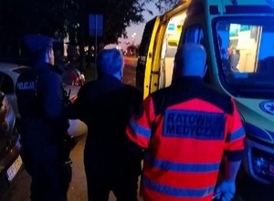 Policjant wraz z ratownikiem prowadzi seniora do karetki.