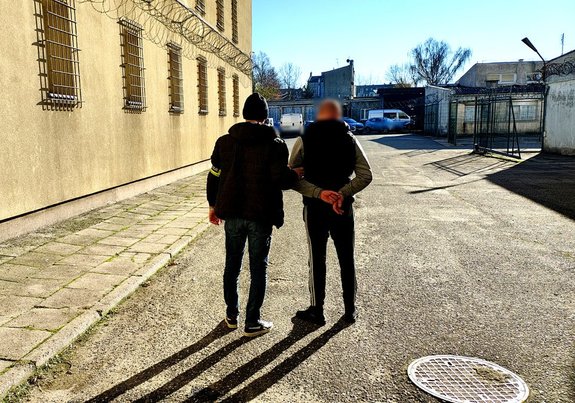 Policjant wraz z zatrzymanym na dziedzińcu Komendy Miejskiej Policji w Piotrkowie Trybunalskim.