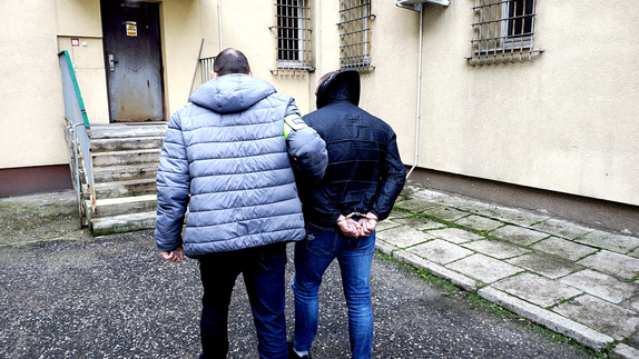 Policjant prowadzący zatrzymanego do pomieszczenia dla osób zatrzymanych.