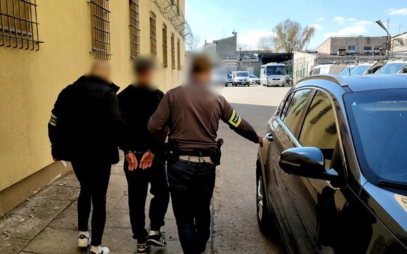 Policjanci trzymający zatrzymanego.