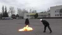 Instruktor rzuca koktajlem mołotowa - butelką z paliwem w manekina ubranego w mundur policyjny. U dołu manekina kula ognia.
