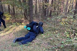 ćwiczenia policjantów w lesie, policjant leży z bronią obserwując teren