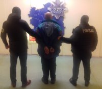 Na zdjęciu mężczyzna zatrzymany przez policjantów. Policjanci trzymają mężczyznę za ręce skute kajdankami. W tle grafika z mapą komisariatów.