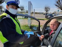 policjantka daje własnoręcznie uszytą maseczkę kierowcy samochodu.