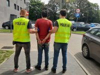 dwóch policjantów trzyma po obu stronach zatrzymanego
