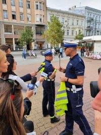 Na zdjęciu , które zostało zrobione na placu Schillera , policjant wraz z policjantką robią pokaz , gdzie prawidłowo umieścić elementy odblaskowe. Na zdjęciu widać również zaproszonych dziennikarzy.