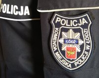 Na mundurze napis POLICJA oraz naszywka z napisem Komenda Miejska Policji w Łodzi a po środku naszywki znajduje się odznaka policyjna z herbem Łodzi
