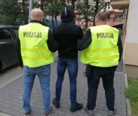 Nieumundurowani policjanci w żółtych kamizelkach z napisem POLICJA prowadzą zatrzymanego sprawce kradzieży