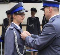 Na zdjęciu jest policjantka, Katarzyna Borowiec podczas wręczania srebrnej odznaki sprawności fizycznej. Kasia jest ubrana w mundur galowy, Jeden z przełożonych wręcza jej odznakę.