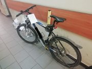 Na zdjęciu widoczny rower koloru niebiesko-czarnego. Rower ustawiony jest pod ścianą w pomieszczeniu Policji.