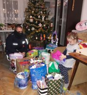 Dziewczynka w otoczeniu prezentów, w tle policjant.