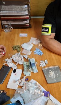 Policjanci podczas ważenia i badania narkotyków. Na stoliku zabezpieczone zawiniątka z folii aluminiowej i pieniądze.