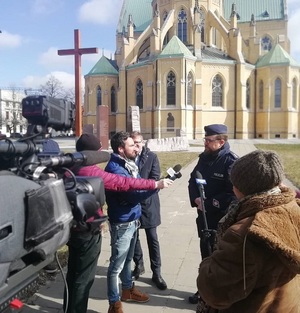 Policjant udziela wywiadu przed kamerą na tle katedry łódzkiej.