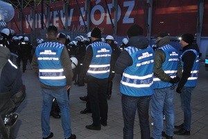 Policjanci skupieni w rejonie wyjścia nadzorują opuszczanie stadionu przez kibiców po zakończonym meczu.