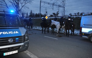 Na jezdni sąsiadującej ze stadionem stoją funkcjonariusze na koniach, po obu stronach radiowozy policyjne.