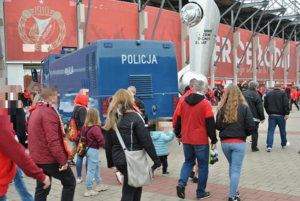 Kibice idący do wejścia stadionu. W tle policyjna armatka wodna.