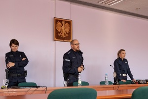 Policjanci biorący udział w spotkaniu stoją za stołem.