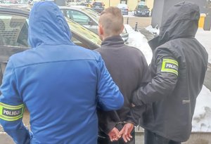 Dwaj nieumundurowani policjanci prowadzą zatrzymanego mężczyznę