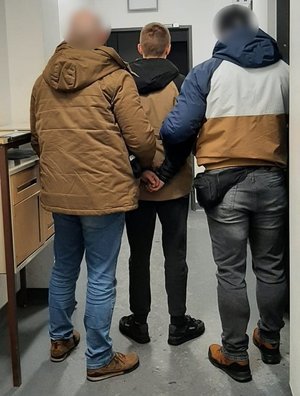 Nieumundurowani policjanci wraz z zatrzymanym idą korytarzem komisariatu.
